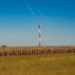 Torre de comunicação instalada em um campo rural sob céu azul.