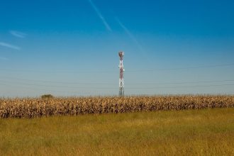 Torre de comunicação instalada em um campo rural sob céu azul.