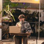 Jovem artista faz leitura de poesia ao ar livre usando um microfone