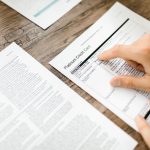 Mão analisando um contrato de cartão de crédito sobre uma mesa de madeira.