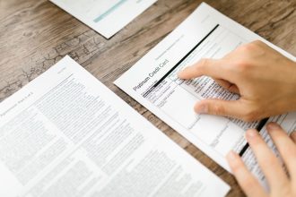 Mão analisando um contrato de cartão de crédito sobre uma mesa de madeira.